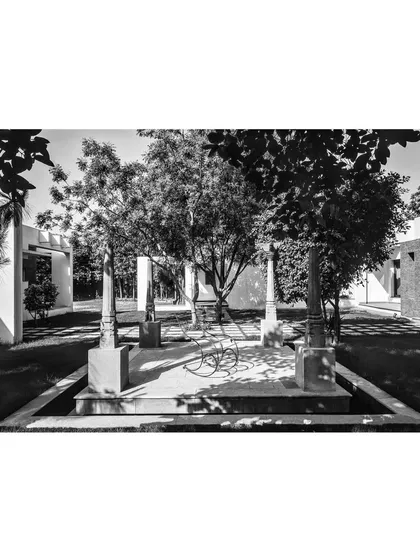 A black and white photograph of the House of Axes, emphasizing the strong geometric forms and the interplay of light and shadow. The design integrates ancient stone columns, establishing a historical identity for the site.
