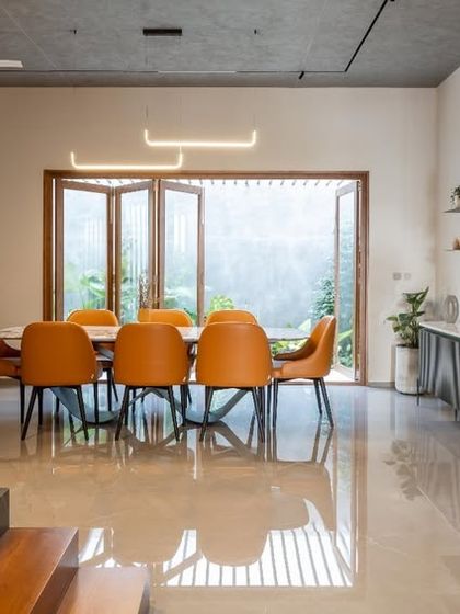 The dining area is designed to be bright and open, connecting directly to the outdoors through foldable glass doors. The wooden staircase and slatted wall partition add warmth and texture, complementing the sleek marble-top dining table.