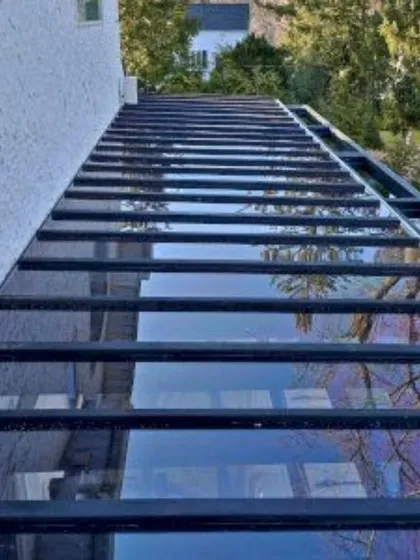 This image shows a long-span glass roof we installed over a walkway. The black metal frame and tinted glass panels provide shelter and a sleek, modern aesthetic, connecting different parts of the property.