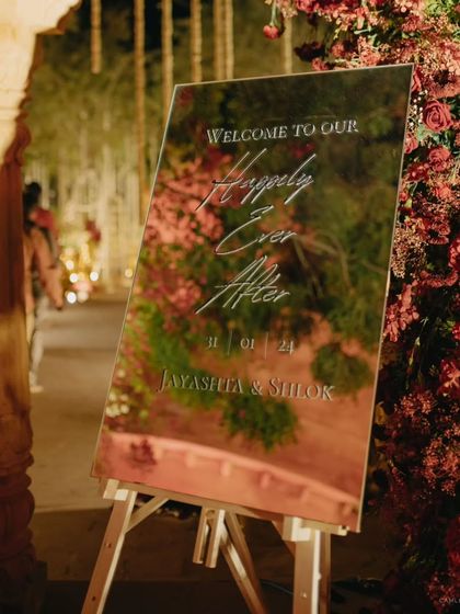 A mirrored welcome sign at the entrance of the wedding venue. It reflects the beautiful floral decor, creating a stunning first impression for guests.