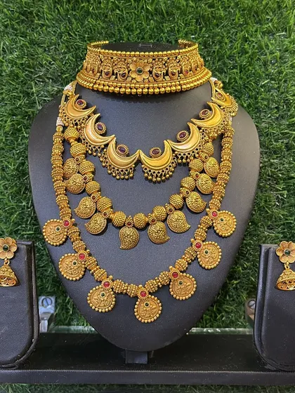 A beautiful gold-finish set featuring a choker, a mid-length necklace with a mango design, and a longer coin necklace.