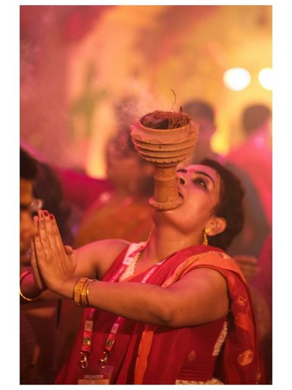 A woman performs the Dhunuchi dance, a ritual where devotees dance with a smoking earthen pot to appease the Goddess Durga. Her expression is one of deep spiritual trance.