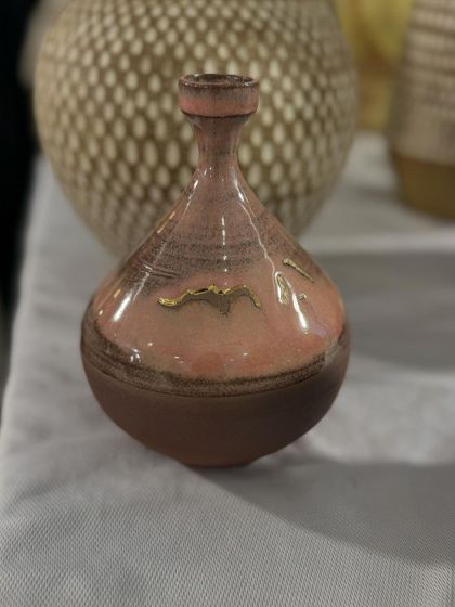 A small, delicate bud vase with a lovely pink and brown glaze, accented with a touch of gold. It's perfect for holding a single stem.