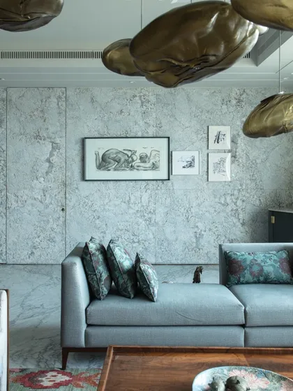 The living room at 'The 42, Kolkata', where a textured stone wall serves as a backdrop for charcoal art and a comfortable lounge sofa. A Bocci clouds light installation adds a dreamy, celestial feel.