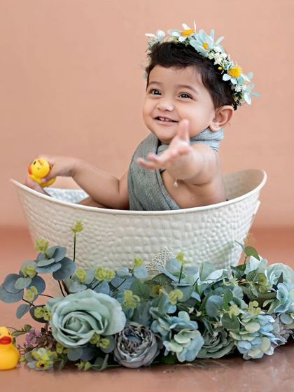 A happy little one waving from the tub, surrounded by rubber ducks and flowers. A classic and adorable tub bath moment.
