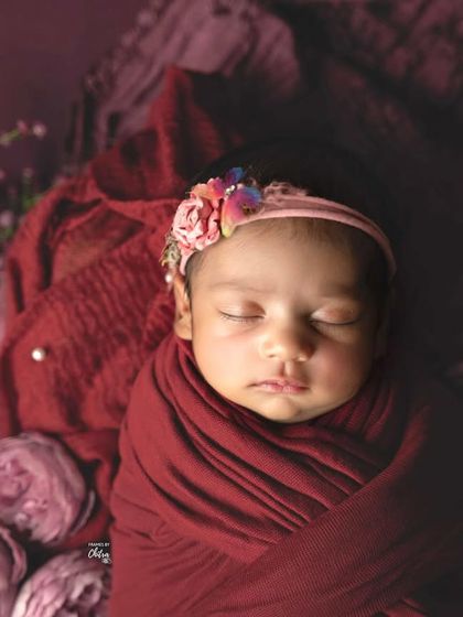 A tight portrait focusing on the baby's face, surrounded by the rich colours and soft textures of the floral arrangement.