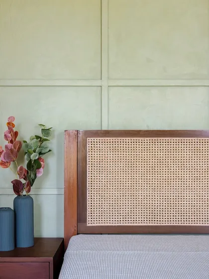 This bedroom features a cane headboard set against a paneled, lime-washed green wall. The combination of textures and soft colors creates a peaceful and inviting retreat.