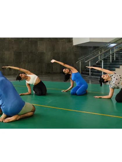 Students follow the instructor in a deep side-body stretch on the floor, an essential part of warming up for our aerial yoga sessions.