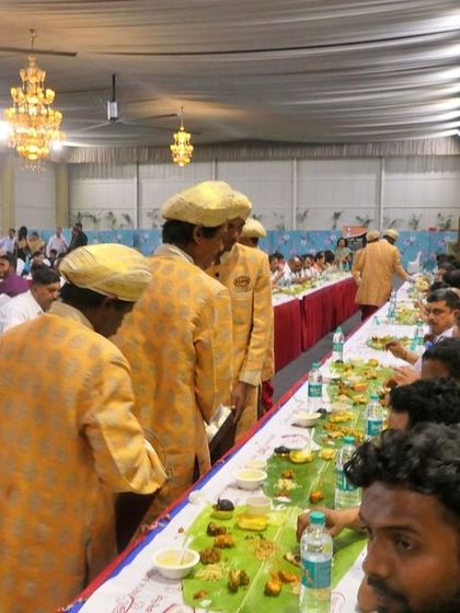 My team, dressed in traditional uniforms, moves efficiently along the dining line to serve guests. This image captures the organized flow of our ela sadya service at a large wedding.