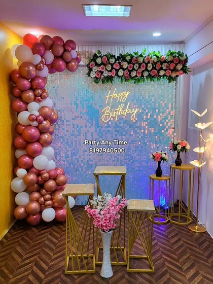 For a touch of glamour, I offer shimmer wall backdrops. This birthday setup combines a sparkling iridescent wall with a balloon garland, a floral arrangement, and modern gold plinths.