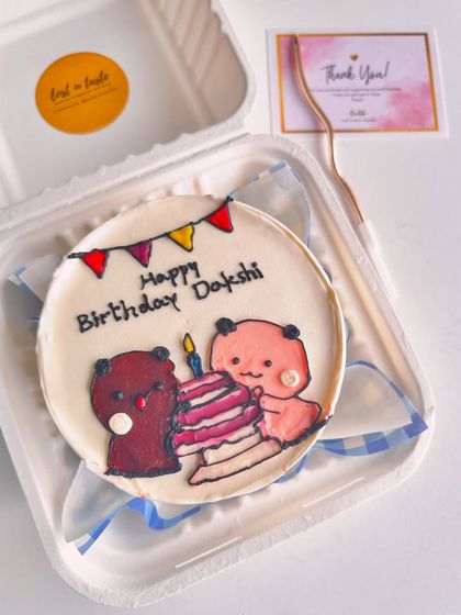 A personalized birthday bento for Dakshi, showing two cute bears celebrating with a layered birthday cake and candle.