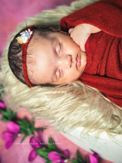 A close-up portrait focusing on the newborn's face. The soft fur, rich red wrap, and delicate headband come together to create a beautiful and detailed shot.