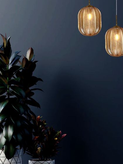 A pair of woven metallic pendants set against a dark, moody wall. The intricate texture of the shades creates a beautiful play of light and shadow, defining luxury through subtle, brilliant details.
