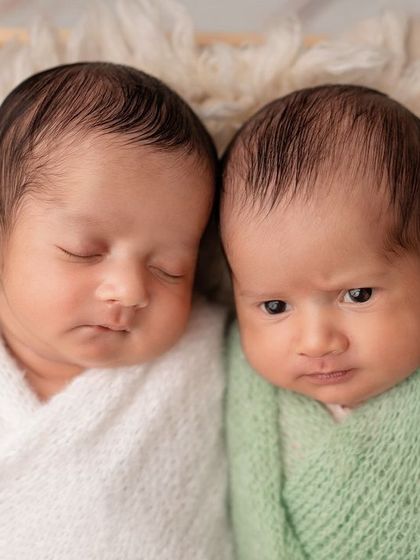 A close-up of newborn twins snuggled together in a wooden crate. One awake and one asleep!