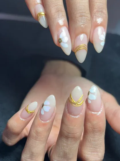 A beautiful set of almond-shaped nails with a milky white base, accented with gold lines and subtle white heart details.