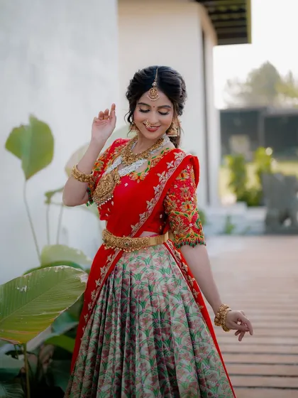 A full-length shot of actress Niveditha Gowda in a traditional half saree. Her pose and the garden setting create an image of grace and elegance.