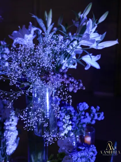 A close-up of the floral arrangements, with delicate baby's breath and lilies bathed in the moody blue light of the event.