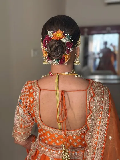 A vibrant floral bun for a bride, using a mix of colorful flowers to match her orange lehenga.