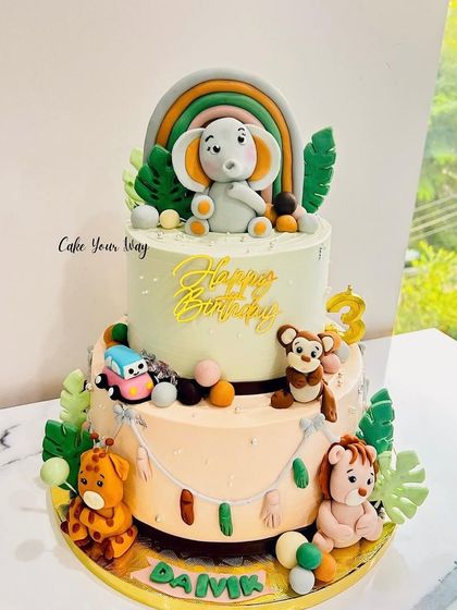The cutest two-tier animal cake, featuring a baby elephant, giraffe, lion, and monkey.