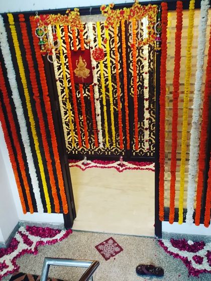 This is a complete entrance decoration for a puja at home. It features hanging marigold garlands and a floor rangoli made of flower petals to welcome guests.
