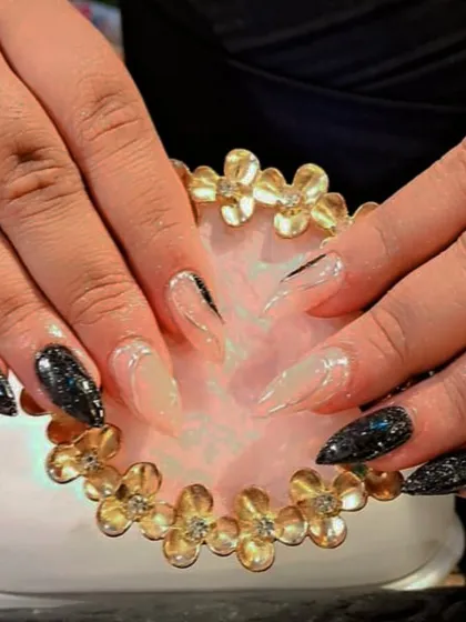 A dramatic set of stiletto nails combining a sheer nude base with black glitter and sharp black line accents.