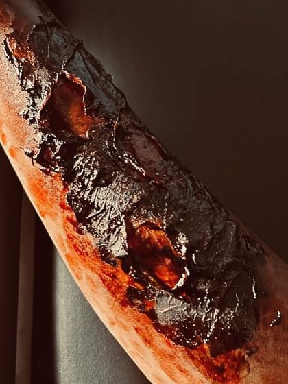 A closer view of the severe burn prosthetic, highlighting the charred and peeling skin effects. The glossy texture mimics freshly damaged tissue, adding to the realism needed for cinematic shots.