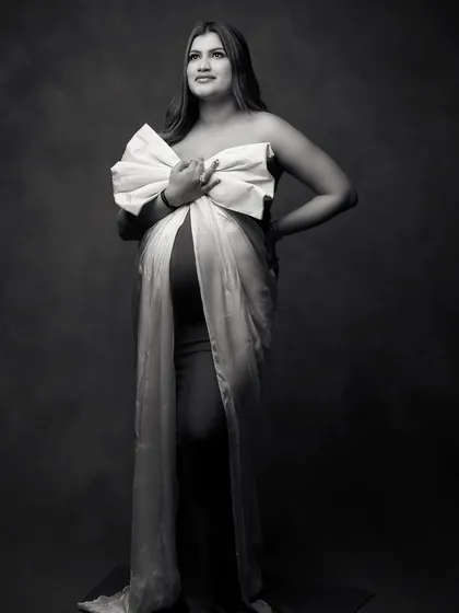 A full-length black and white portrait showcasing the elegant silhouette of the expecting mother. The contrast emphasizes the beautiful shape of the baby bump and the dramatic bow.