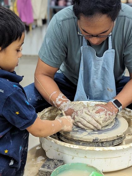 A father and son work together on the potter's wheel, a memorable experience from one of our weekend workshops.
