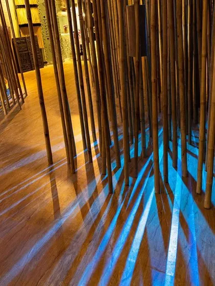 The play of light and shadow in the 'Edge of the Forest' bamboo installation. The cool blue light contrasts with the warm wood tones, creating a serene and contemplative mood.