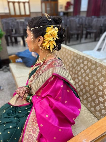 A view of the traditional bridal bun adorned with yellow flowers and a hair accessory, perfectly complementing her green and pink saree.