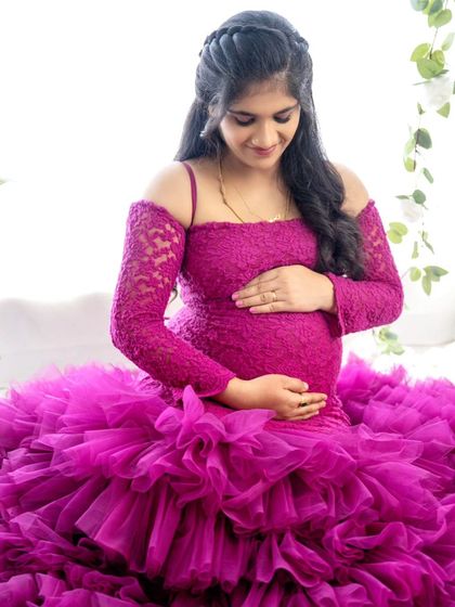 A beautiful portrait of a mom-to-be seated in a magenta ruffled gown, looking down at her baby bump with love.