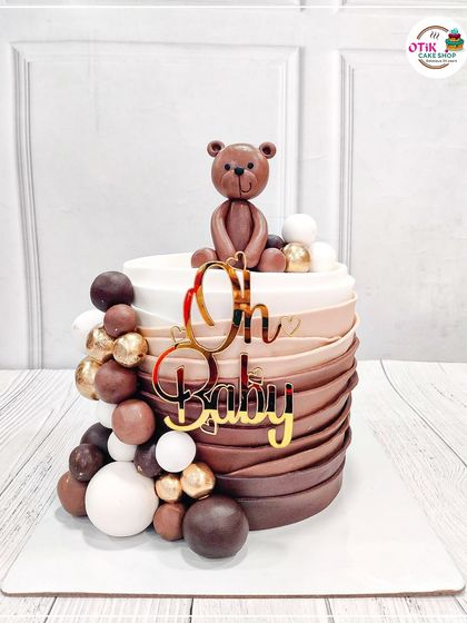 A chic and modern baby shower cake with a cascade of brown and white chocolate spheres. The cute fondant teddy bear on top adds a touch of sweetness.