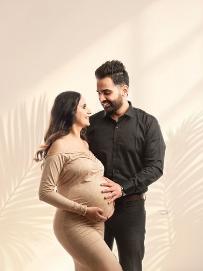A tender moment shared between partners, both gently holding the baby bump. The coordinated neutral outfits and soft lighting create a warm and loving atmosphere.