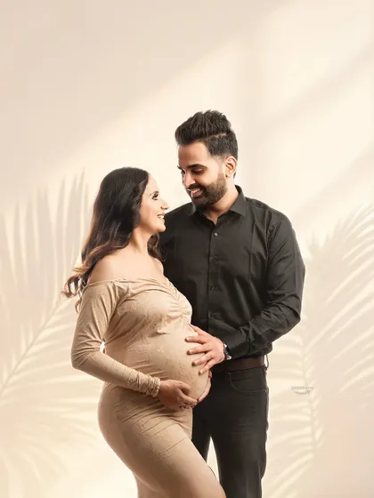 A tender moment shared between partners, both gently holding the baby bump. The coordinated neutral outfits and soft lighting create a warm and loving atmosphere.
