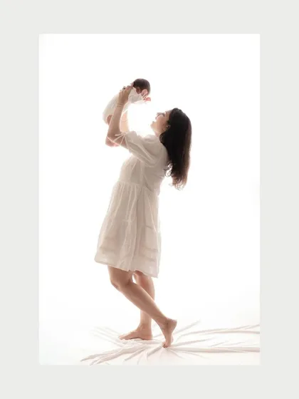A mother joyfully lifts her newborn baby up in a bright, high-key studio setting. Her silhouette is filled with light, creating an ethereal and uplifting image that symbolizes the joy of new life.