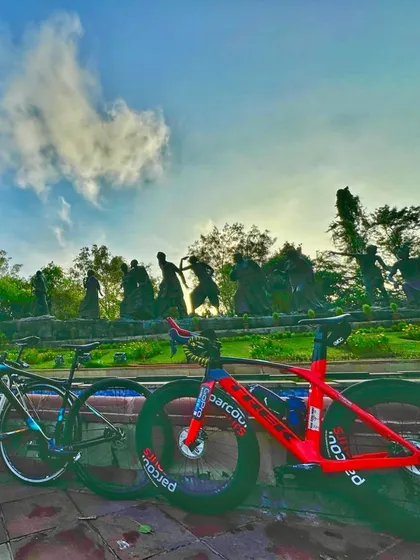 A creative shot of two bikes parked in front of the Gyarah Murti sculpture.