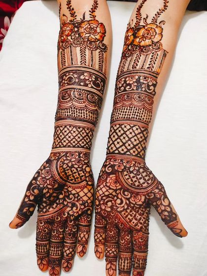 This bridal henna design features beautiful floral bands at the cuff, with detailed grid work and patterns extending down to the fingertips.