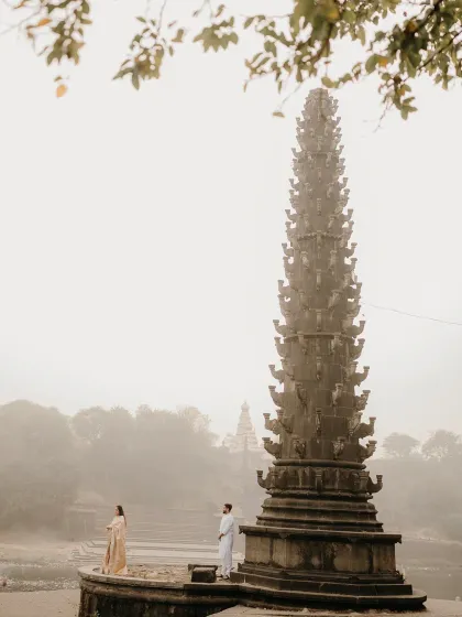 Standing by a 'deepstambh' in the morning mist. This atmospheric shot captures a sense of peace and devotion, reflecting a love that is deep and spiritual.