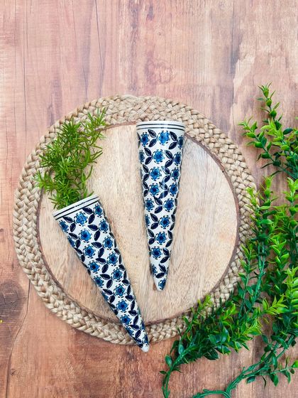 A close-up of our hand-painted ceramic conical wall planters in a dark blue floral design. These are perfect for water plants and add a touch of elegance to any wall.
