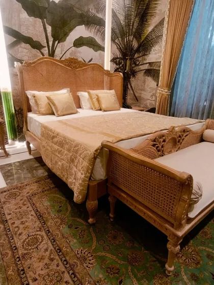 This bedroom set has a royal, vintage feel. The bed, side table, and divan are all crafted from light-colored wood with beautiful, ornate carvings and cane accents.