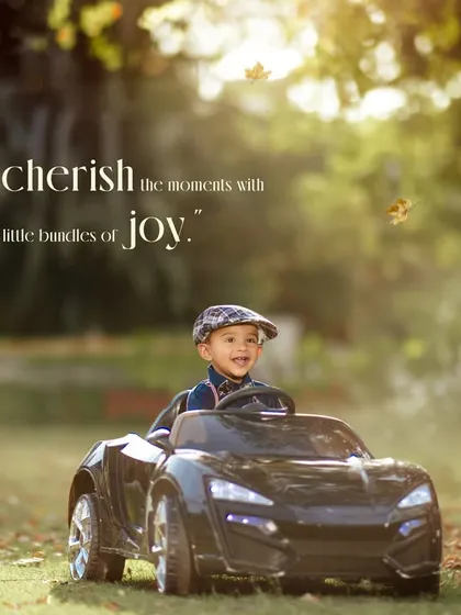 An outdoor portrait capturing a happy toddler enjoying a ride in a sleek black toy car. We love using natural golden hour light to create these warm, cherished memories in a park setting.