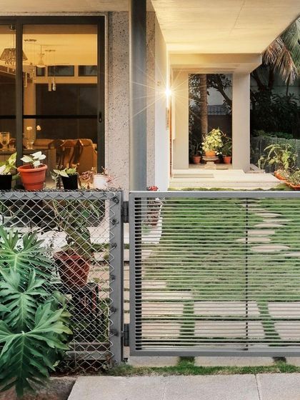 The entrance to "Casa Magnifera," showing a modern gate and a simple stone path leading to the front door. The design balances security and openness, offering a welcoming glimpse into the home.