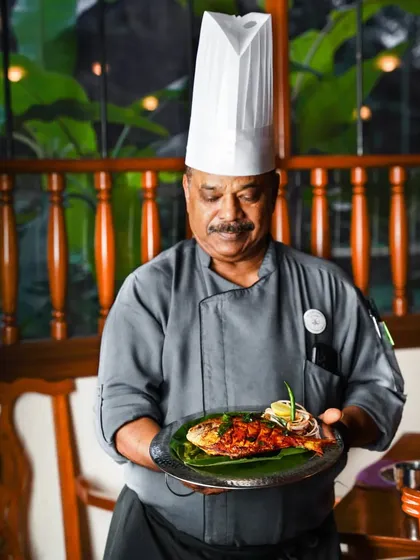 A proud chef in his uniform, holding a plate of perfectly cooked fish. This portrait captures the experience and tradition he brings to his coastal cuisine restaurant.
