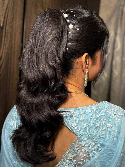 The hairstyle was a chic, high ponytail with soft waves, adorned with delicate pearl accessories.