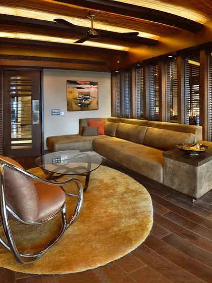 A cozy den in the Magnolias project, featuring a comfortable sectional sofa and a unique rocking chair. The wood-slatted walls and ceiling create a warm, cabin-like feel.