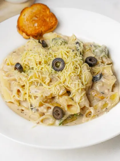 A serving of creamy alfredo penne pasta with olives and a generous topping of cheese. The bright, clean lighting makes this classic comfort dish look extra inviting.