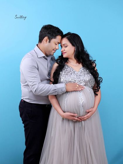 An intimate couple portrait against a solid blue background. The husband's gentle touch and their close embrace create a simple yet powerful image of their connection.