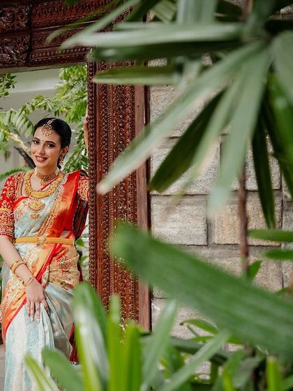 A bride, framed by lush green leaves, looks out from an antique doorway, a beautiful and natural portrait.