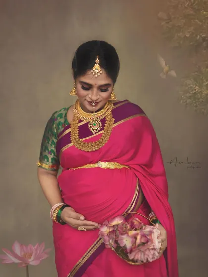 A close-up portrait focusing on the mother's gentle gaze towards her baby bump. The rich temple jewelry and vibrant saree make this a stunning example of a cultural maternity photoshoot.