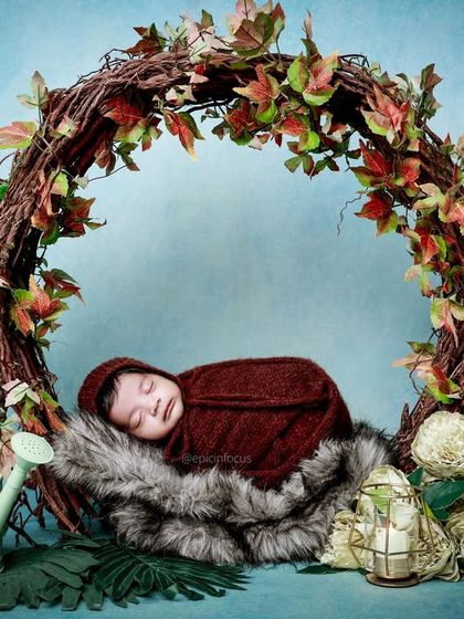 A baby in a rich, maroon wrap nestled inside a rustic wreath of vines and autumn leaves. This setup is perfect for a fall-themed newborn shoot.